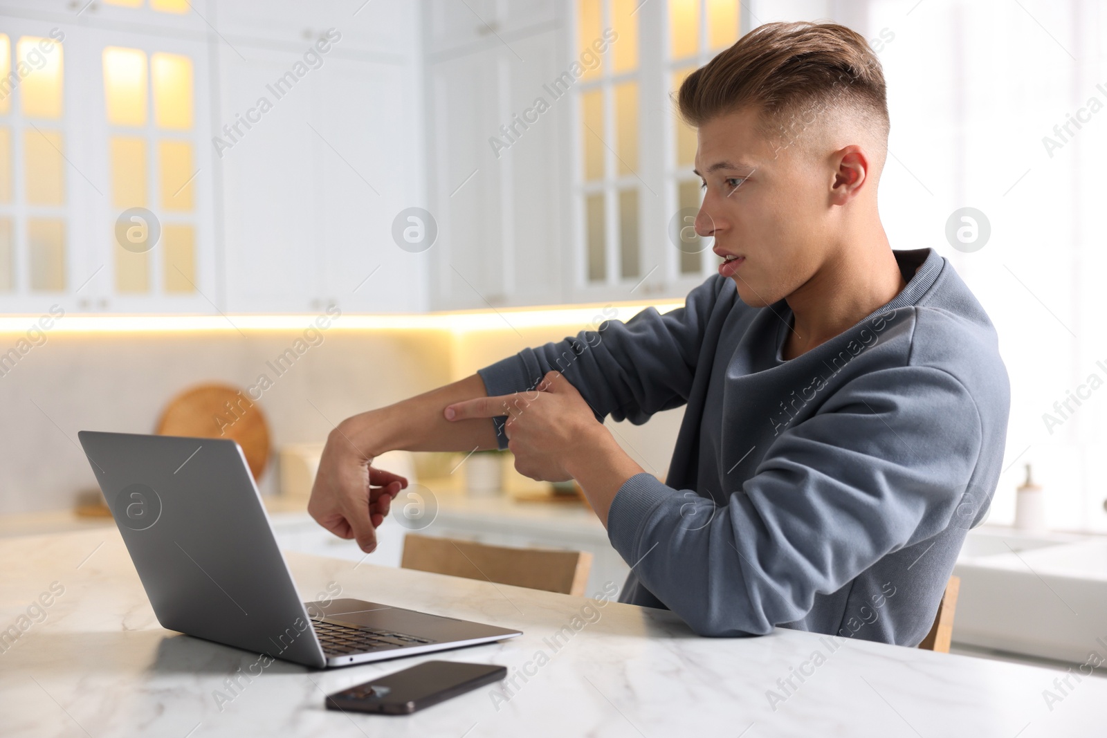 Photo of Sick man having online consultation with doctor via laptop at white marble table in kitchen
