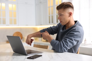 Photo of Sick man having online consultation with doctor via laptop at white marble table in kitchen
