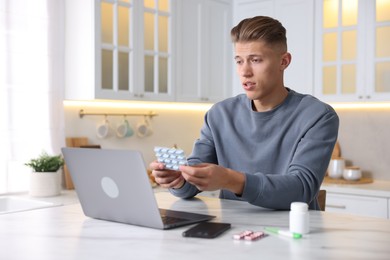Photo of Sick man with pills having online consultation with doctor via laptop at white marble table in kitchen