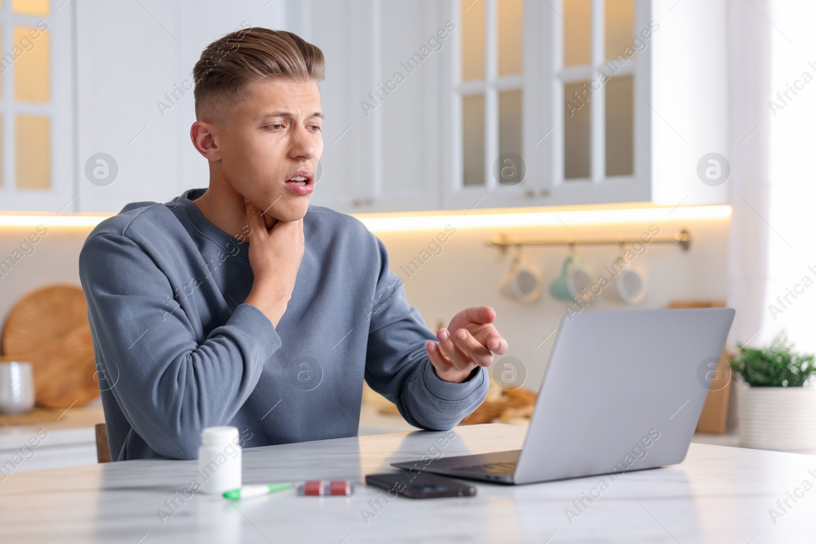 Photo of Sick man having online consultation with doctor via laptop at white marble table in kitchen