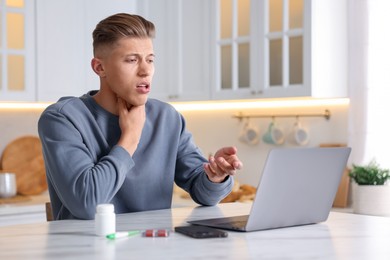 Photo of Sick man having online consultation with doctor via laptop at white marble table in kitchen