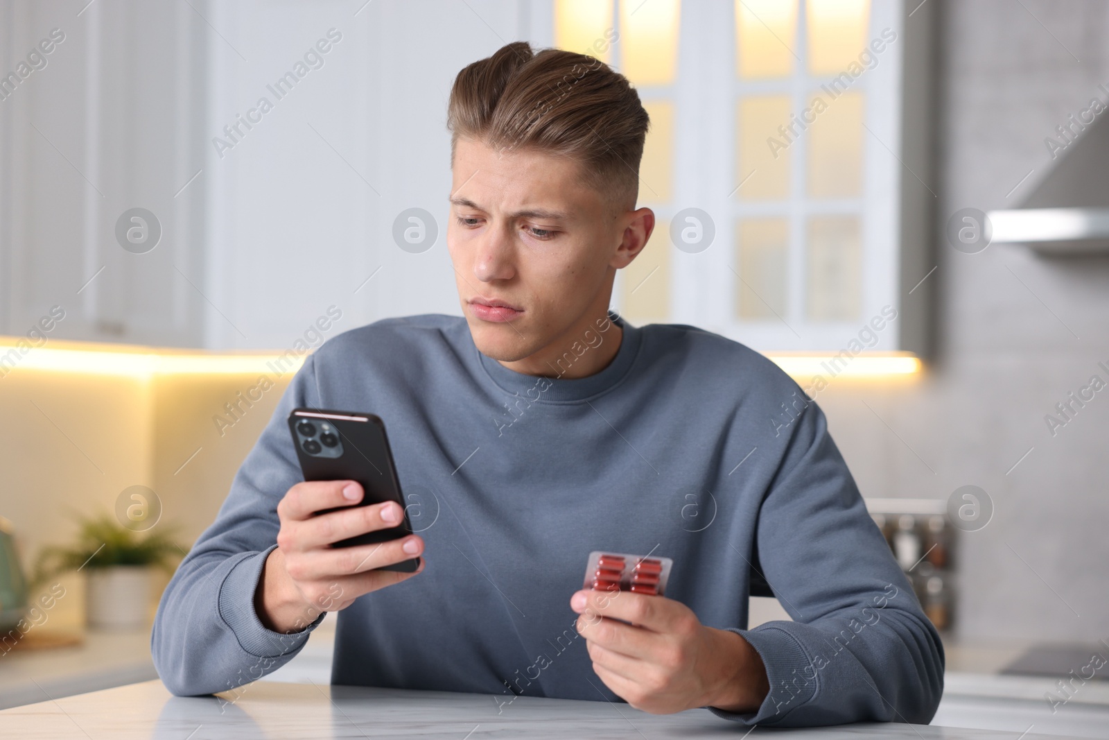 Sick man with pills having online consultation with doctor via smartphone at white marble table in kitchen Photo of Sick man with pills having online consultation with doctor via smartphone at white marble table in kitchen