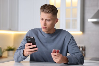 Photo of Sick man with pills having online consultation with doctor via smartphone at white marble table in kitchen