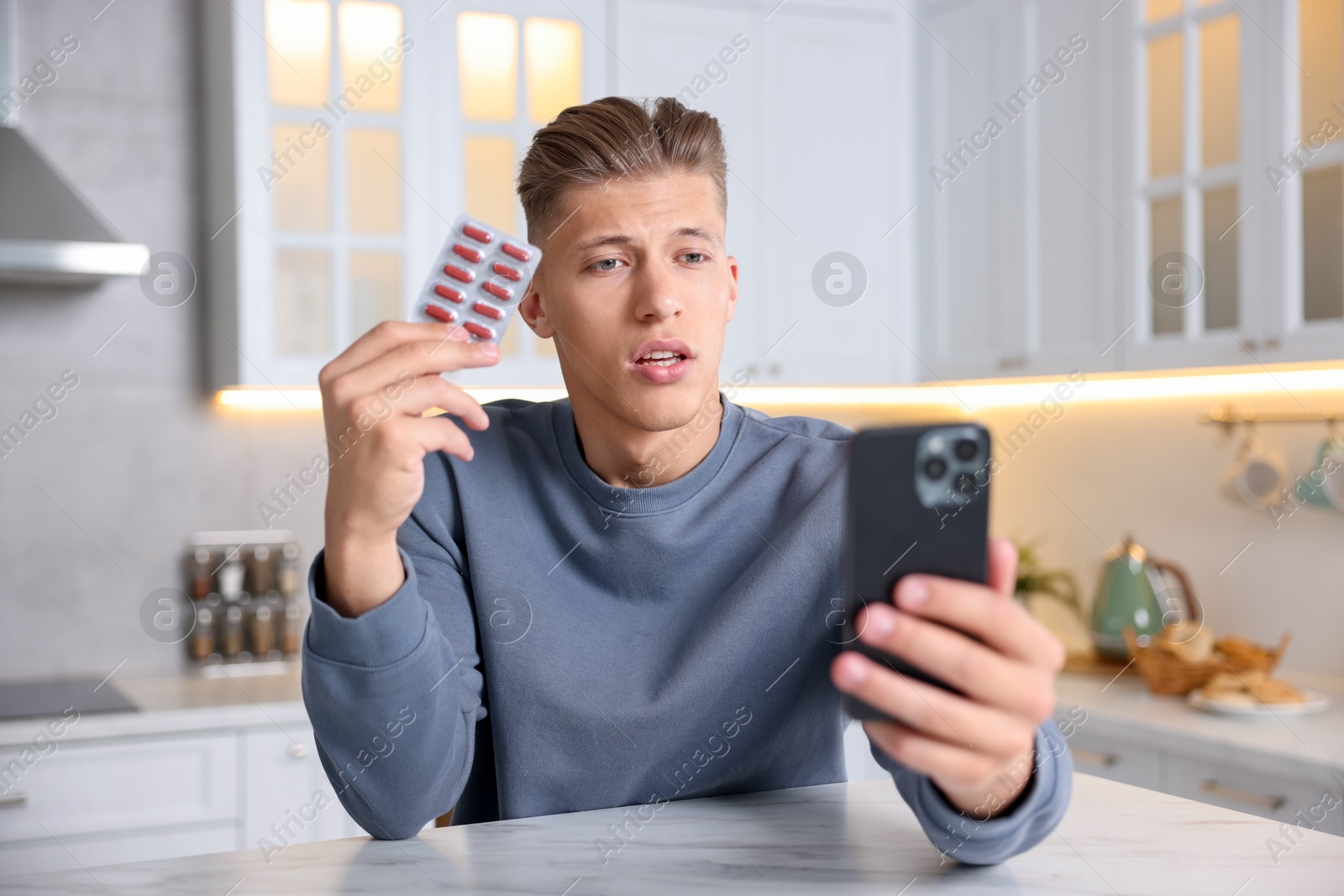 Sick man with pills having online consultation with doctor via smartphone at white marble table in kitchen Photo of Sick man with pills having online consultation with doctor via smartphone at white marble table in kitchen