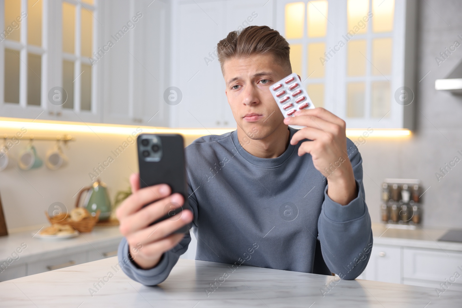 Photo of Sick man with pills having online consultation with doctor via smartphone at white marble table in kitchen