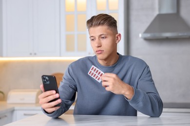 Photo of Sick man with pills having online consultation with doctor via smartphone at white marble table in kitchen