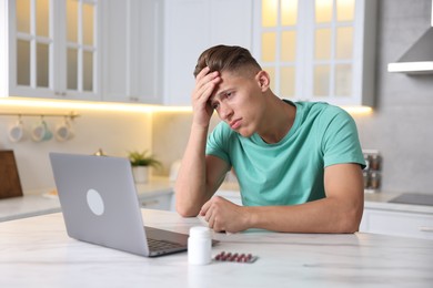 Photo of Sick man having online consultation with doctor via laptop at white marble table in kitchen