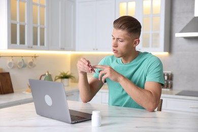 Photo of Sick man with pills having online consultation with doctor via laptop at white marble table in kitchen