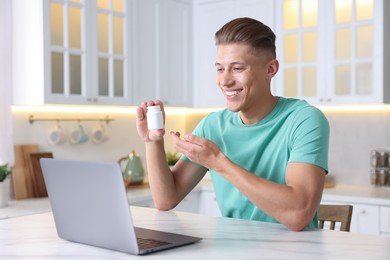 Photo of Sick man with pills having online consultation with doctor via laptop at white marble table in kitchen