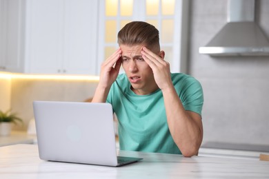 Photo of Sick man having online consultation with doctor via laptop at white marble table in kitchen
