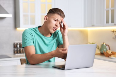 Photo of Sick man having online consultation with doctor via laptop at white marble table in kitchen