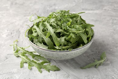Photo of Fresh ripe green arugula leaves in bowl on grey table, closeup