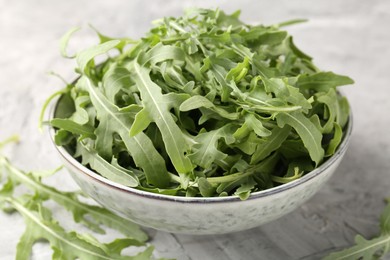Photo of Fresh ripe green arugula leaves in bowl on grey table, closeup