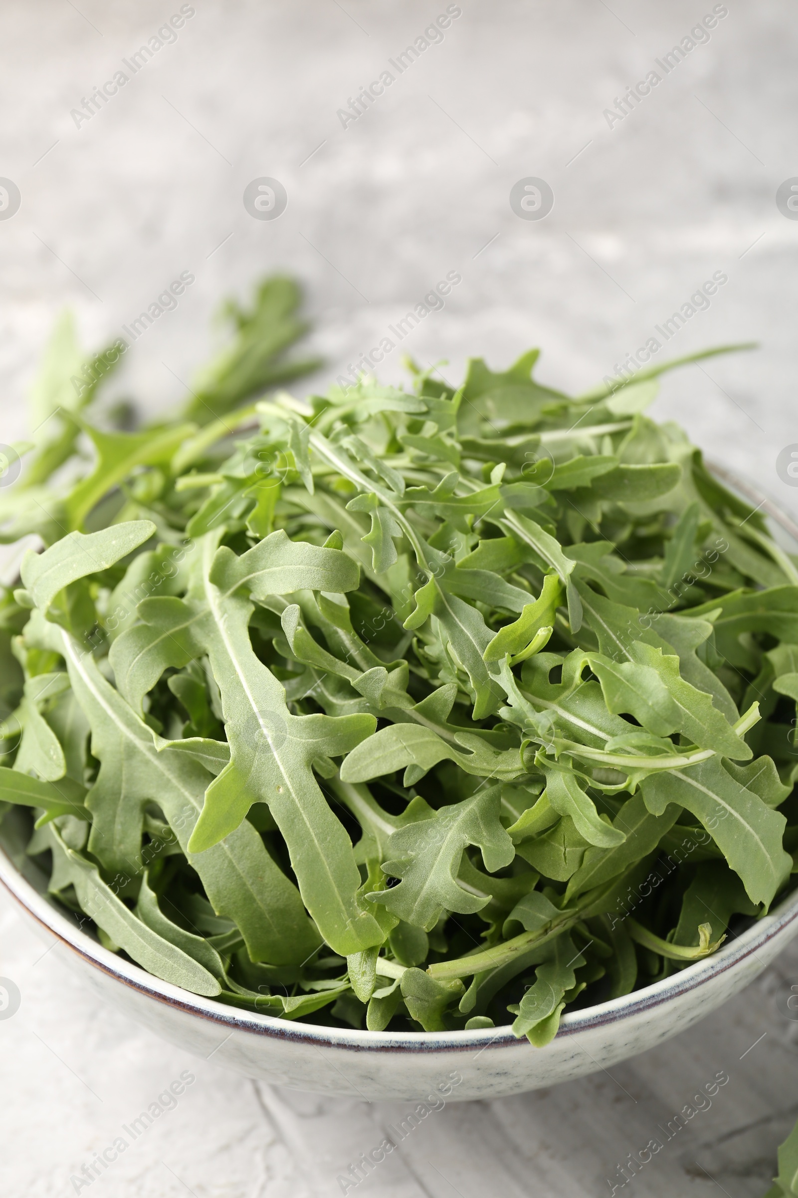 Photo of Fresh ripe green arugula leaves in bowl on grey table, closeup