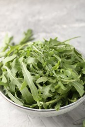 Photo of Fresh ripe green arugula leaves in bowl on grey table, closeup