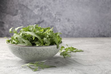 Photo of Fresh ripe green arugula leaves in bowl on grey table, closeup. Space for text