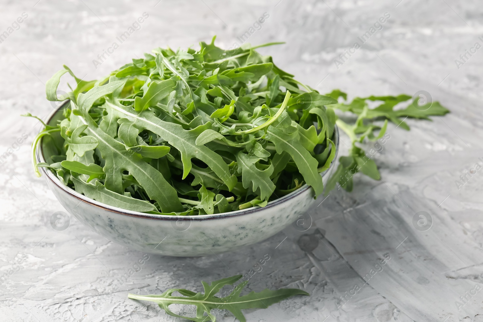Fresh ripe green arugula leaves in bowl on grey table, closeup Photo of Fresh ripe green arugula leaves in bowl on grey table, closeup