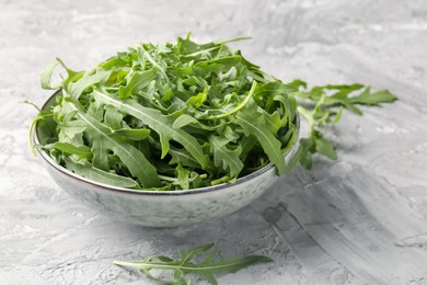 Photo of Fresh ripe green arugula leaves in bowl on grey table, closeup