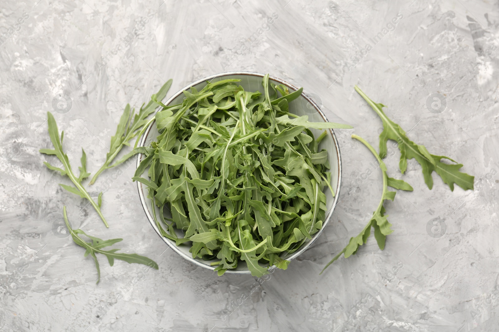 Photo of Fresh ripe green arugula leaves in bowl on grey table, flat lay