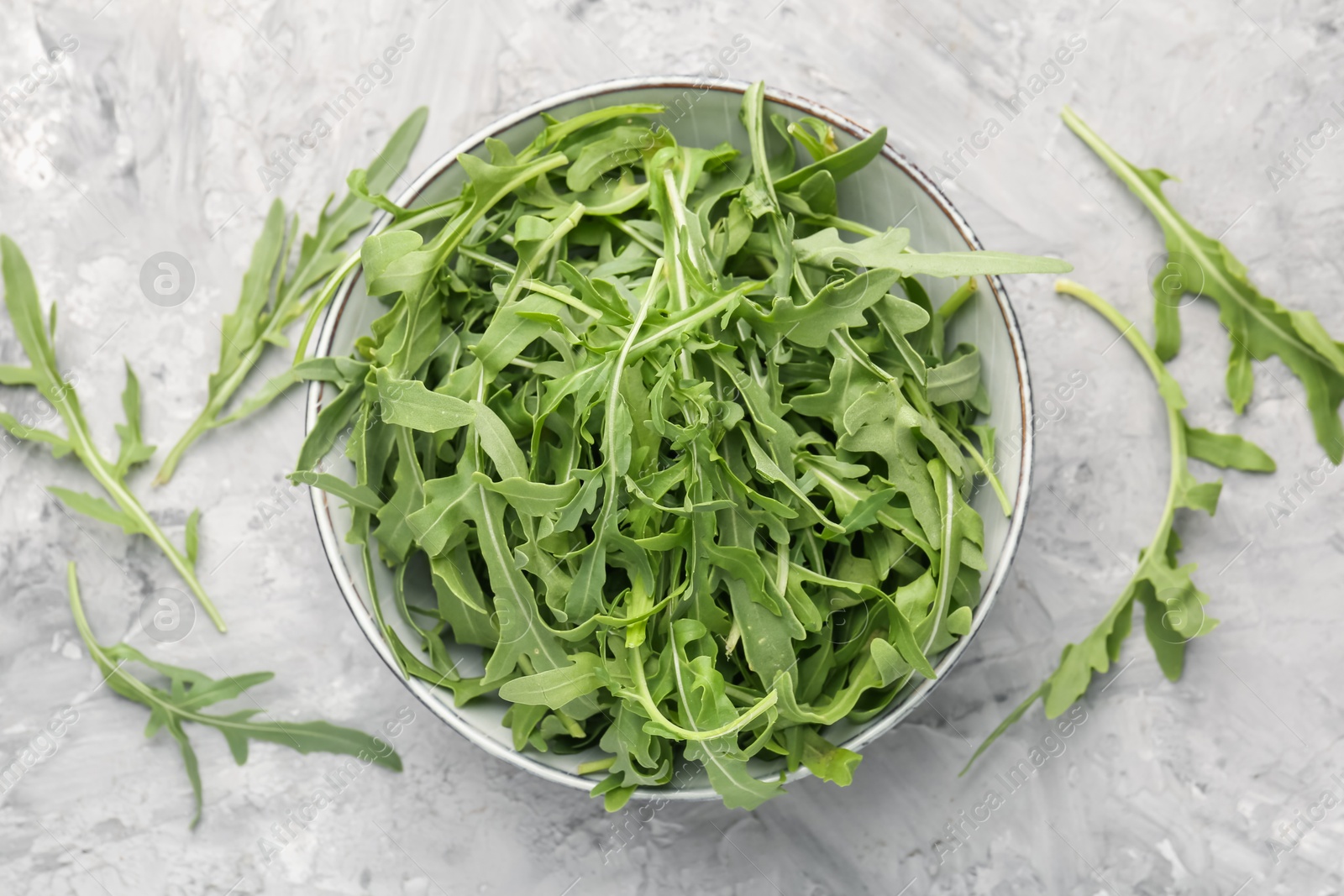 Fresh ripe green arugula leaves in bowl on grey table, flat lay Photo of Fresh ripe green arugula leaves in bowl on grey table, flat lay