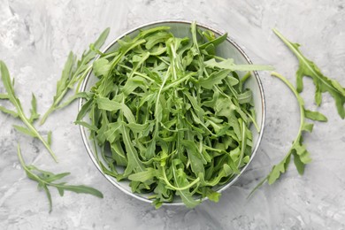Photo of Fresh ripe green arugula leaves in bowl on grey table, flat lay