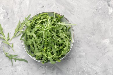 Photo of Fresh ripe green arugula leaves in bowl on grey table, flat lay. Space for text
