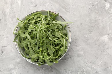 Photo of Fresh ripe green arugula leaves in bowl on grey table, top view. Space for text