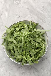 Photo of Fresh ripe green arugula leaves in bowl on grey table, top view