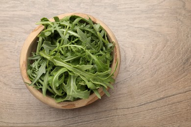 Photo of Fresh ripe green arugula leaves in bowl on wooden table, top view. Space for text