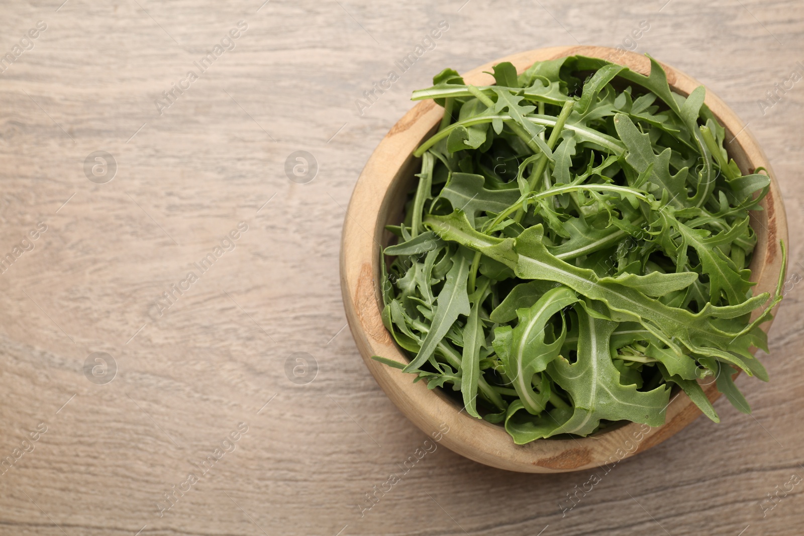 Photo of Fresh ripe green arugula leaves in bowl on wooden table, top view. Space for text