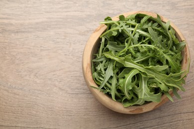 Photo of Fresh ripe green arugula leaves in bowl on wooden table, top view. Space for text