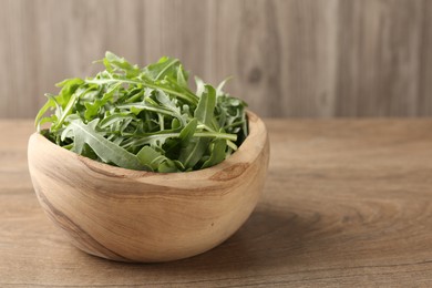 Photo of Fresh ripe green arugula leaves in bowl on wooden table, closeup. Space for text