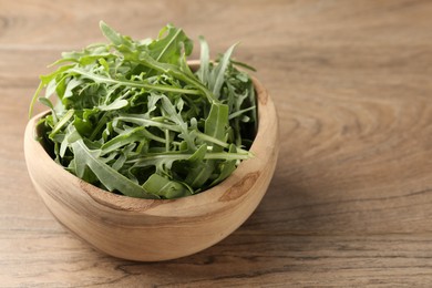 Photo of Fresh ripe green arugula leaves in bowl on wooden table, closeup. Space for text