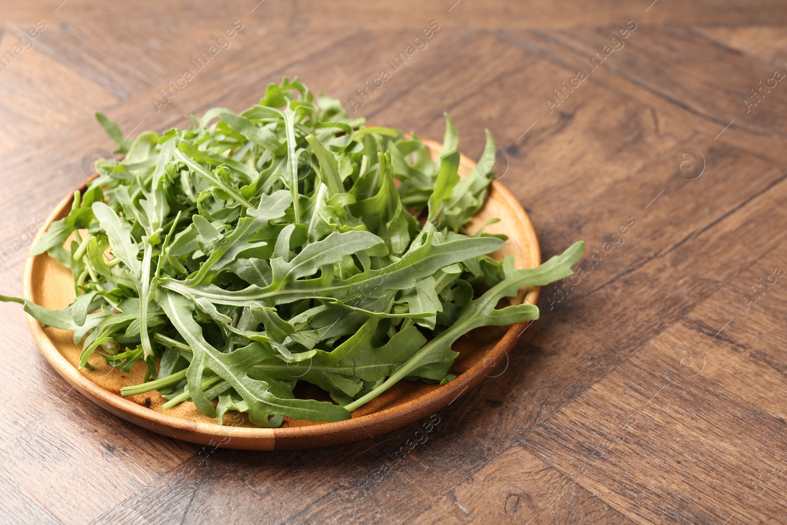 Photo of Fresh ripe green arugula leaves on wooden table, closeup. Space for text