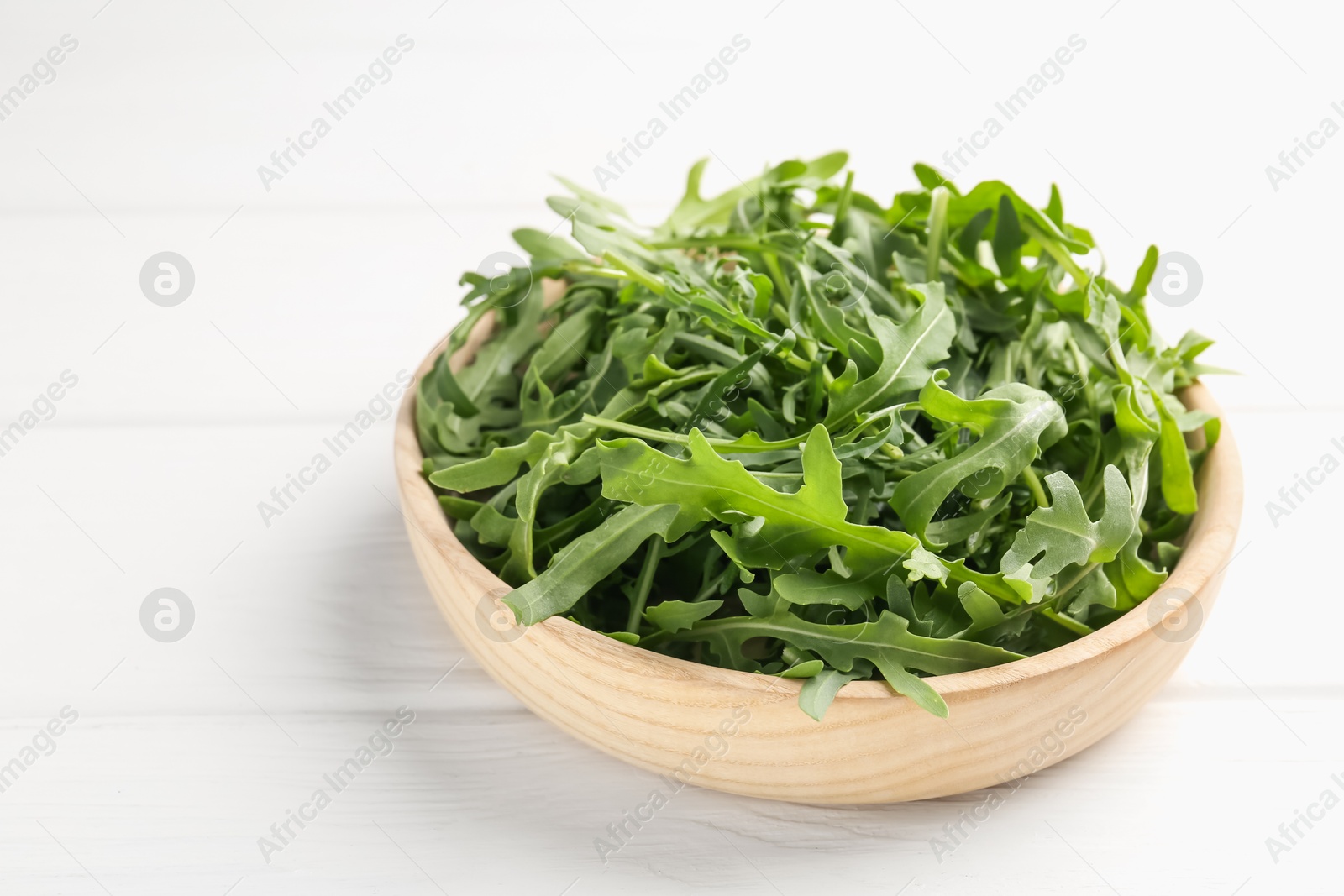 Photo of Fresh ripe green arugula leaves on white wooden table, closeup. Space for text