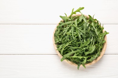 Photo of Fresh ripe green arugula leaves on white wooden table, top view. Space for text