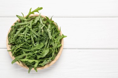 Photo of Fresh ripe green arugula leaves on white wooden table, top view. Space for text