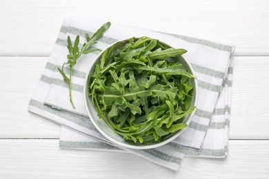 Photo of Fresh ripe green arugula leaves in bowl on white wooden table, top view