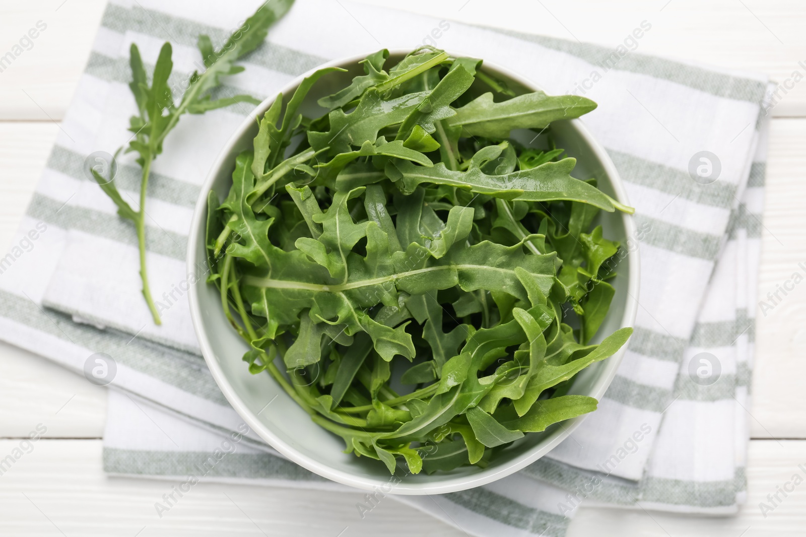 Fresh ripe green arugula leaves in bowl on white wooden table, top view Photo of Fresh ripe green arugula leaves in bowl on white wooden table, top view