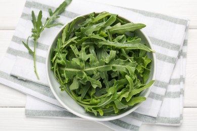 Photo of Fresh ripe green arugula leaves in bowl on white wooden table, top view