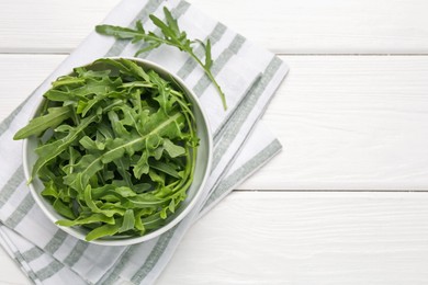 Photo of Fresh ripe green arugula leaves in bowl on white wooden table, top view. Space for text