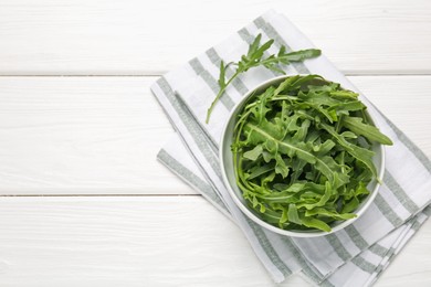 Photo of Fresh ripe green arugula leaves in bowl on white wooden table, top view. Space for text