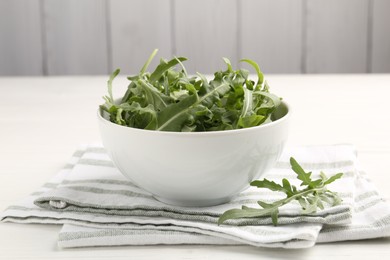 Photo of Fresh ripe green arugula leaves in bowl on white wooden table, closeup