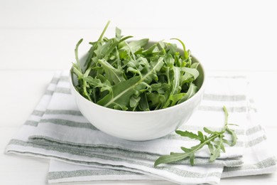Photo of Fresh ripe green arugula leaves in bowl on white table, closeup