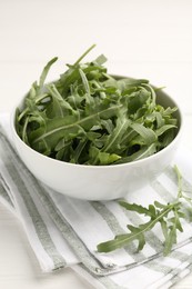 Photo of Fresh ripe green arugula leaves in bowl on white table, closeup