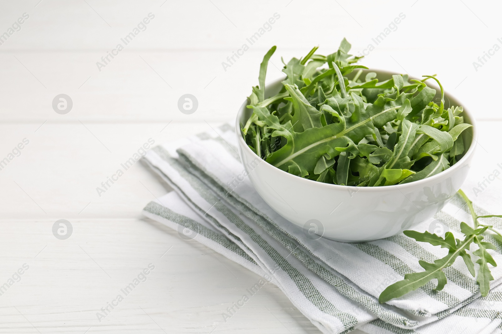 Fresh ripe green arugula leaves in bowl on white wooden table, closeup. Space for text Photo of Fresh ripe green arugula leaves in bowl on white wooden table, closeup. Space for text