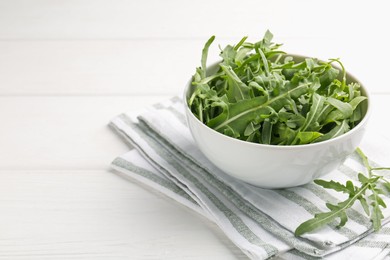 Photo of Fresh ripe green arugula leaves in bowl on white wooden table, closeup. Space for text
