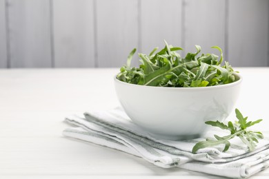 Photo of Fresh ripe green arugula leaves in bowl on white wooden table, closeup. Space for text