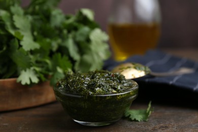 Photo of Tasty cilantro sauce in bowl on wooden table, closeup