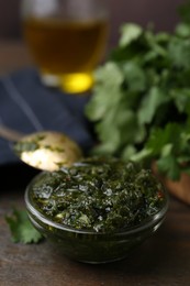 Photo of Tasty cilantro sauce in bowl on wooden table, closeup